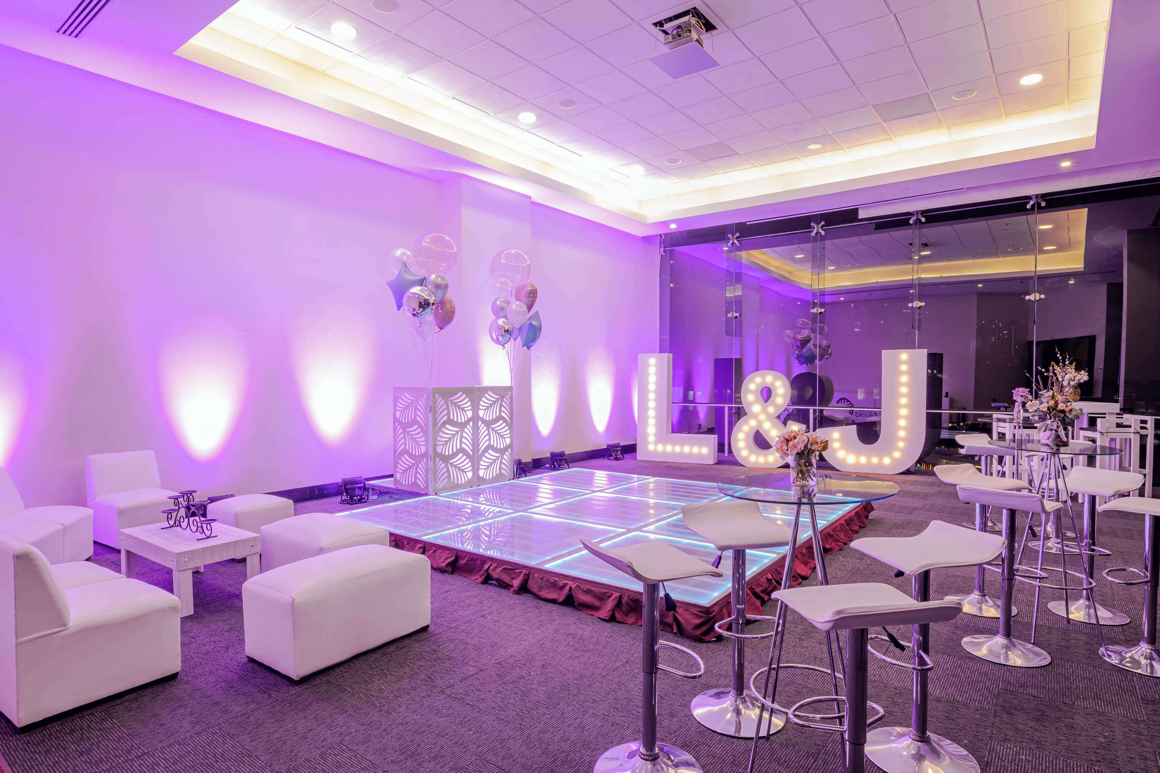 Une salle avec une piste de danse, des canapés blancs et des tabourets de bar.