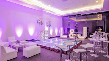 A room with a dance floor, white sofas, and bar stools.