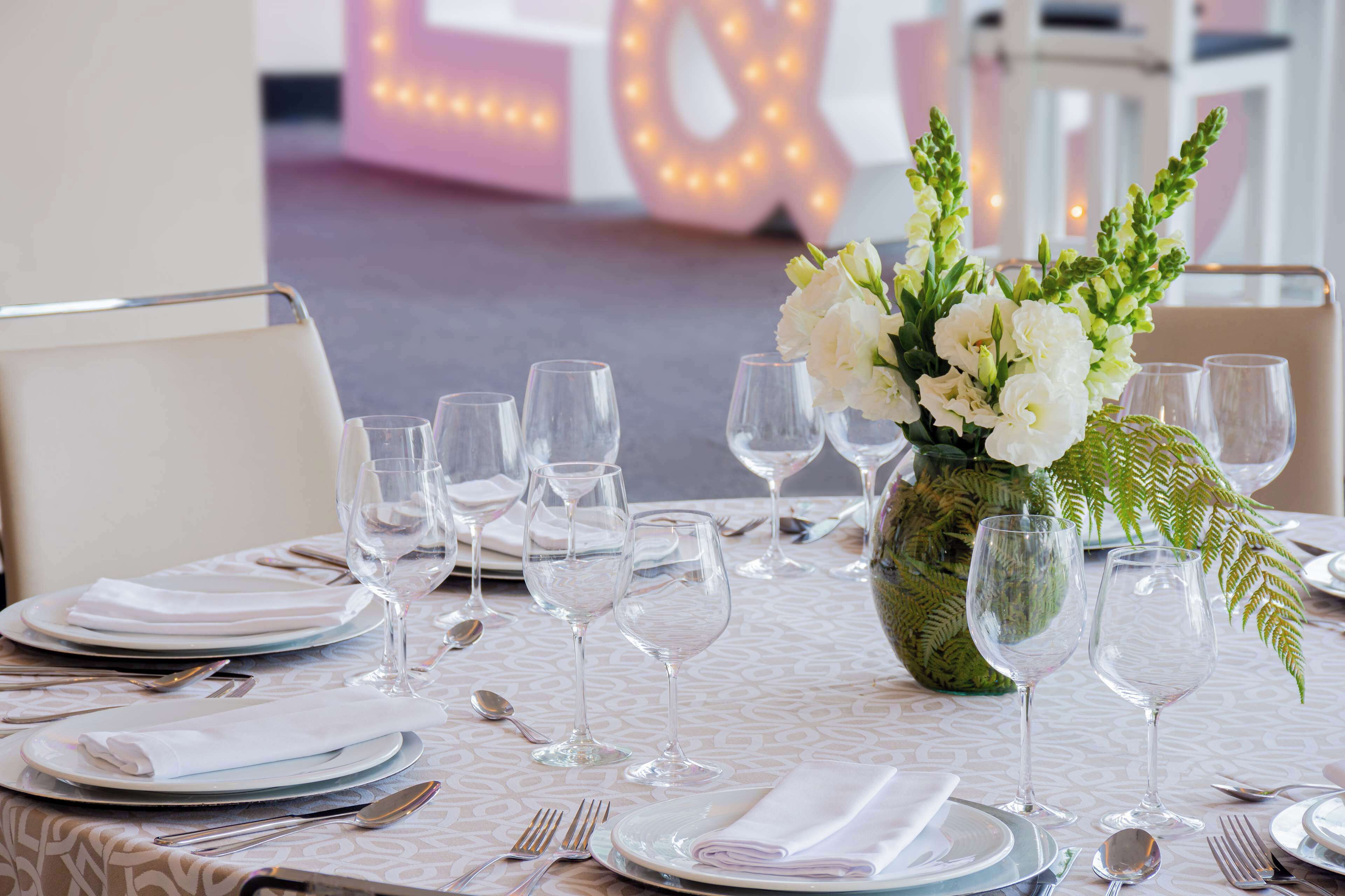 Une table dressée pour un repas formel, avec de l’argenterie, des couverts et de la vaisselle blanche, ainsi qu’un centre de table composé de fleurs.