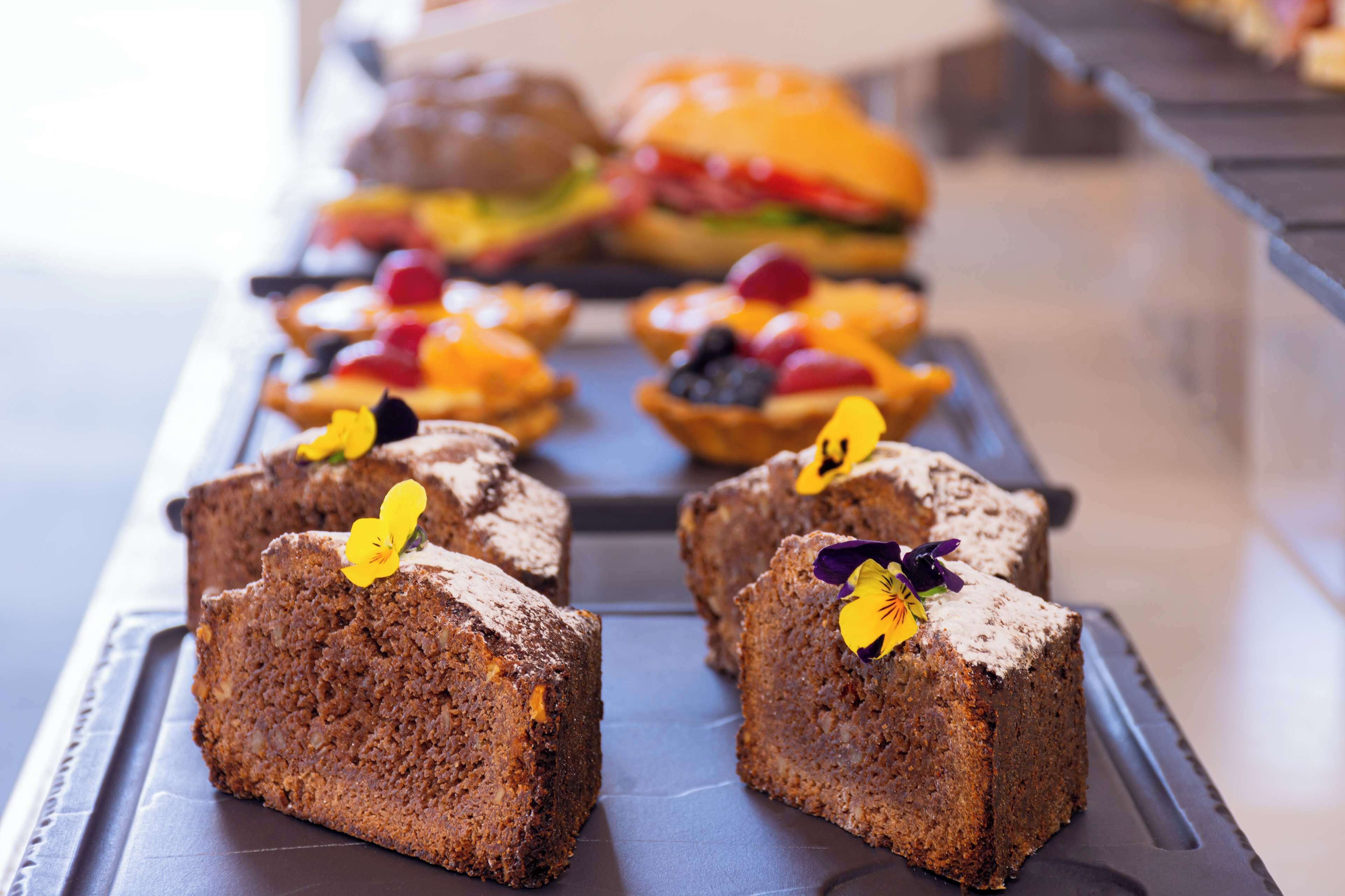 A tray of square-shaped cakes with a flower garnish, placed on a dark surface.