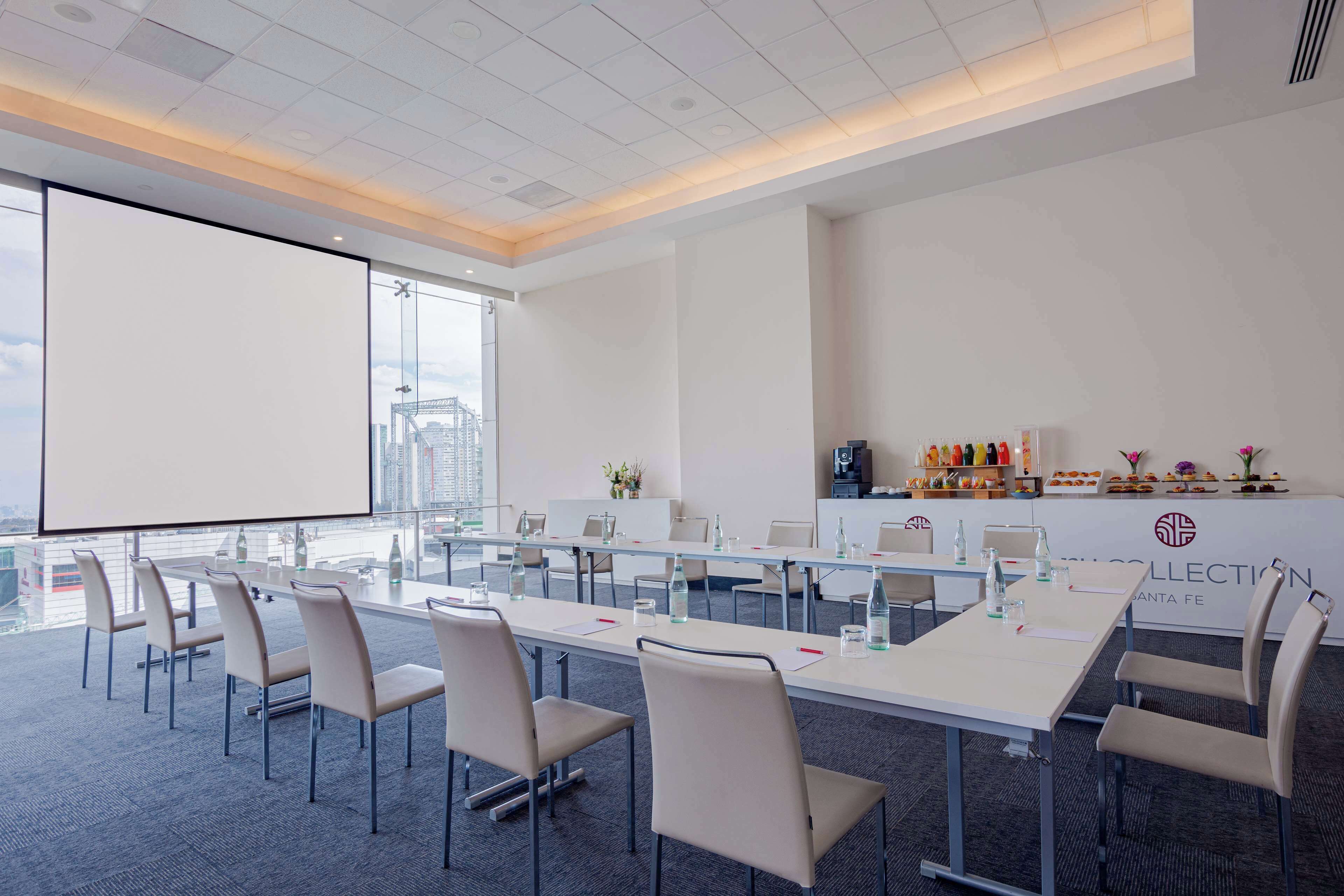 A conference room with a long table, chairs, a projector screen, and a city view.