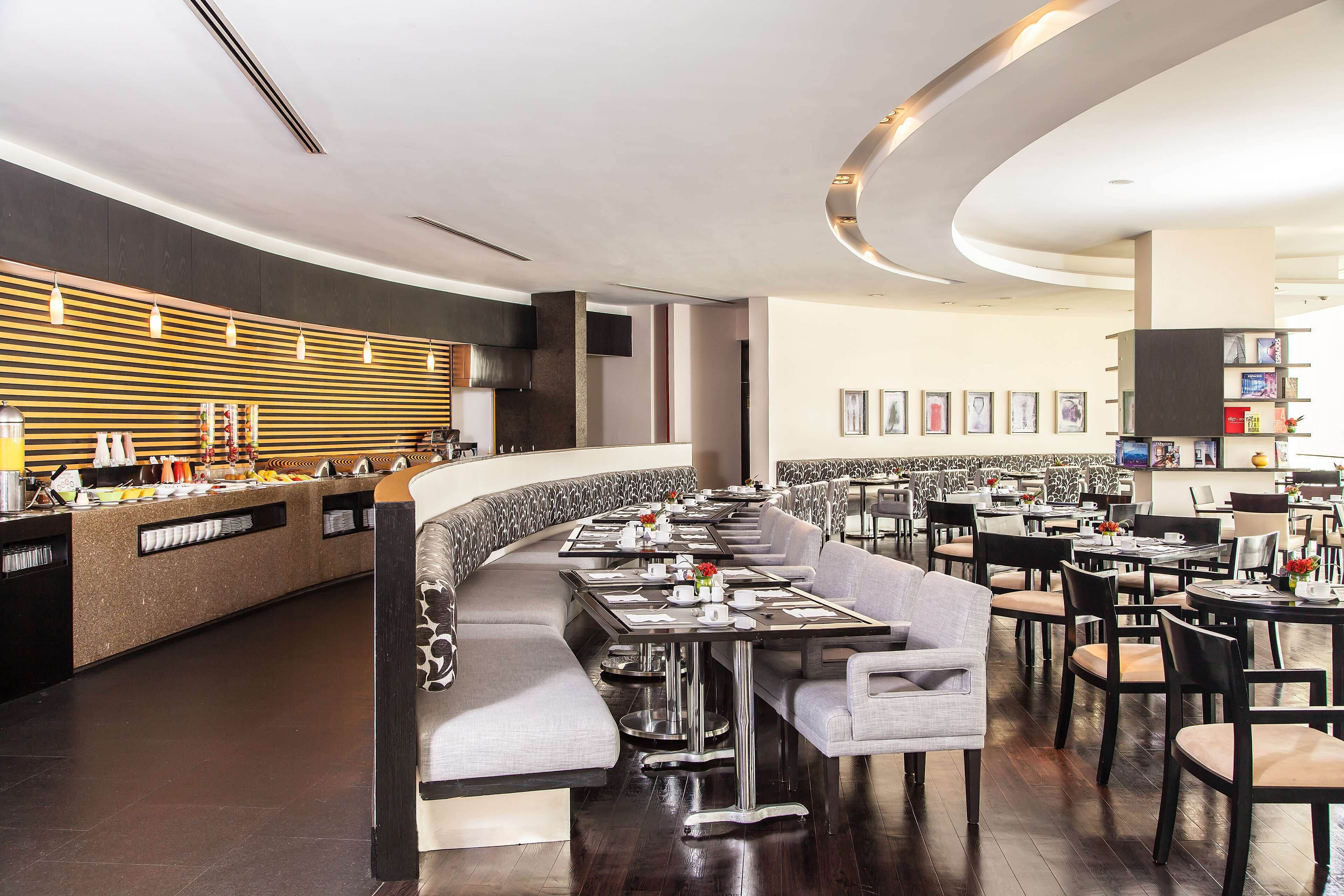 A modern restaurant with a curved counter, seating along the walls, and a mix of tables and booths.