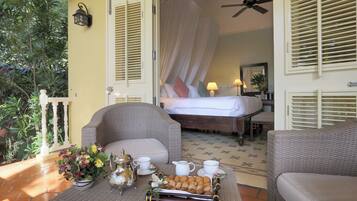 Una habitación con cama, un área de estar con mesa y un balcón con plantas.