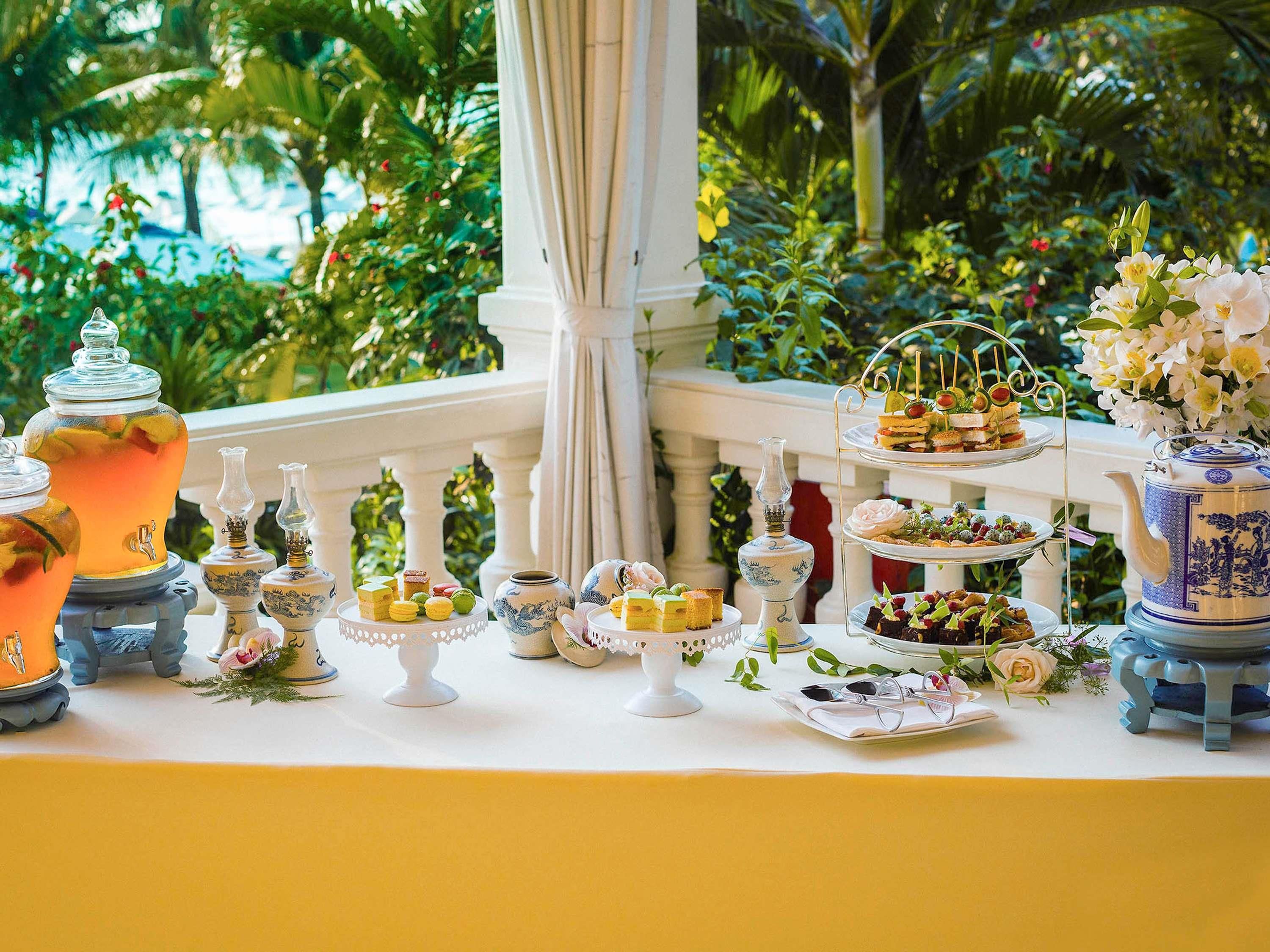 A buffet table with various food items and decorative elements, set against a lush garden backdrop.