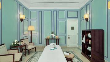 Classic design room with a long bed, two chairs, and a small table with a lamp and vase.