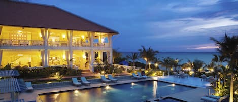 Un resort con piscina, sillones de descanso y vista al océano al atardecer.