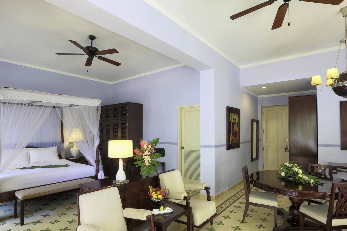 Ein Hotelzimmer mit Bett, Schreibtisch, Esstisch, Stühlen, Deckenventilator und einer Tür.