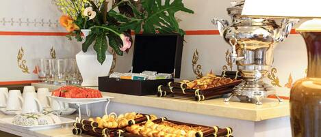 A buffet setup with various food items, a coffee machine, and a decorative plant.