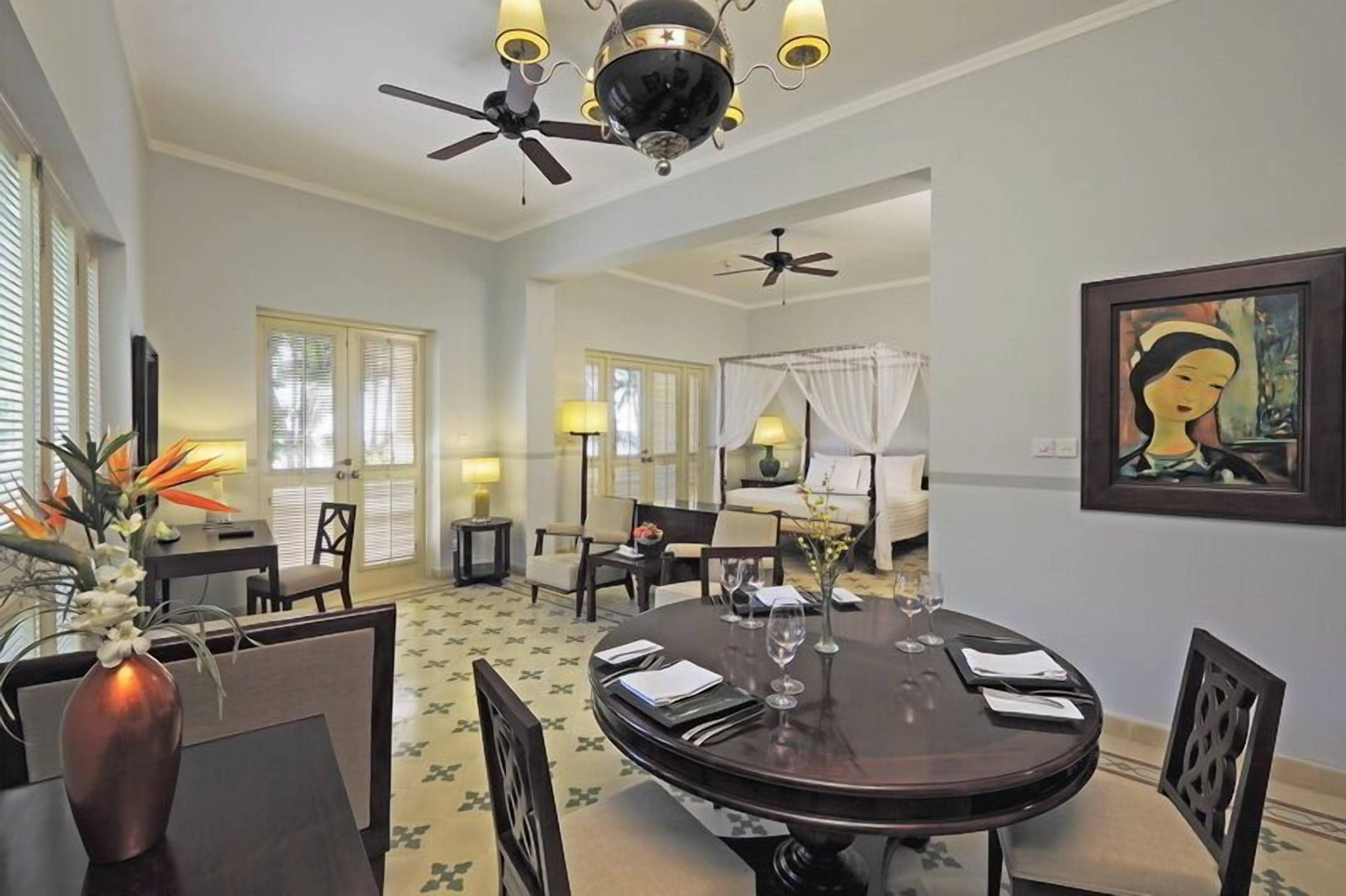 A dining area with a round table, chairs, a vase with flowers, and a ceiling fan.