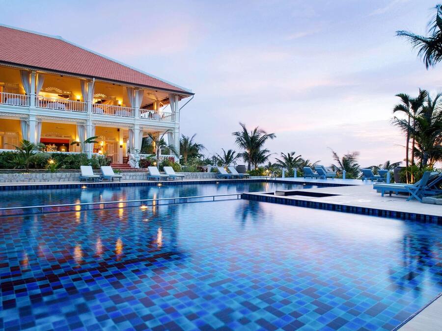 A resort with a swimming pool, lounge chairs, and a building with a red roof.