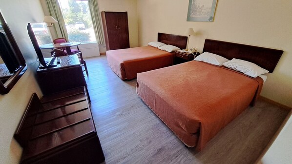 Habitación de hotel con dos camas, un escritorio y una silla. Cuenta con una ventana con cortinas, una puerta y un cuadro en la pared.