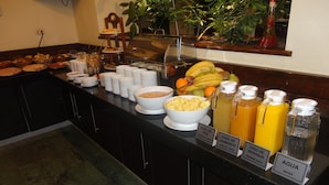 A buffet with various food items and beverages, including bowls of cereal, fruits, and labeled juice dispensers.