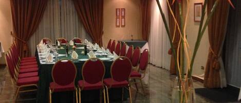 A conference room with a long table set for a meeting, red chairs, and a large vase with tall plants.
