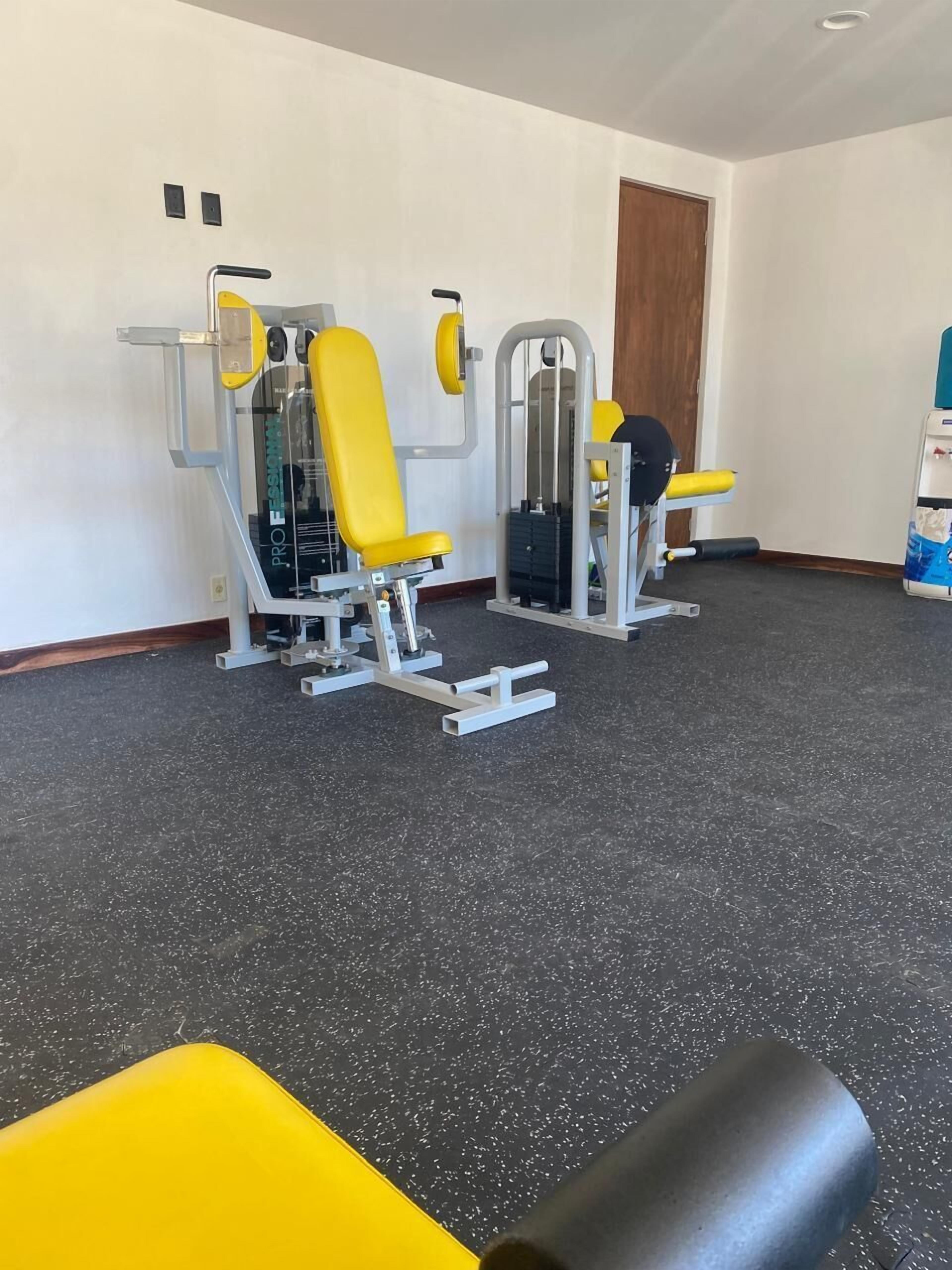 Een fitnessruimte met trainingsapparatuur, waaronder krachttoestellen en een bank.
