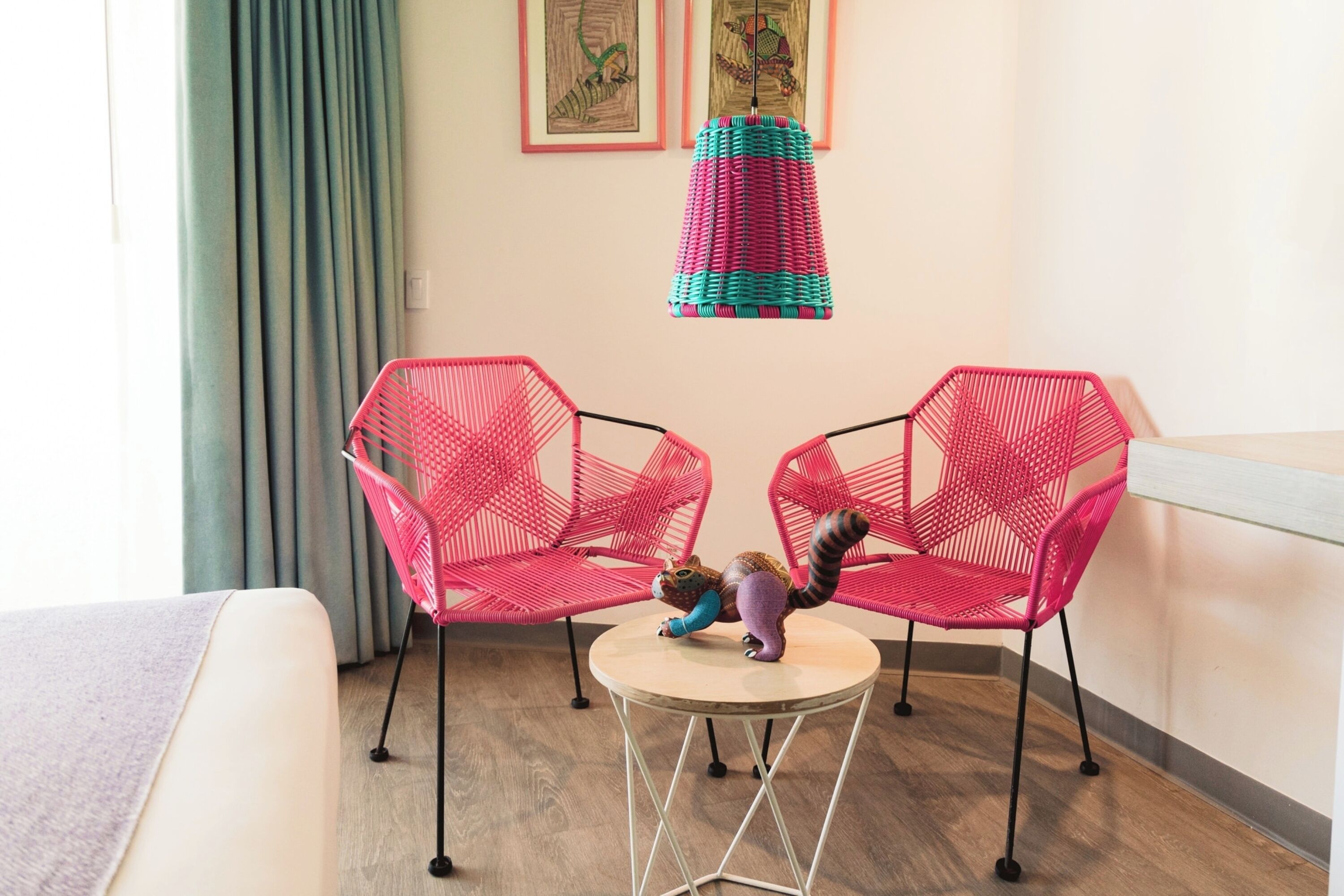Una habitación con dos sillas rojas tejidas, una mesita redonda y un adorno colgante con motivos coloridos.