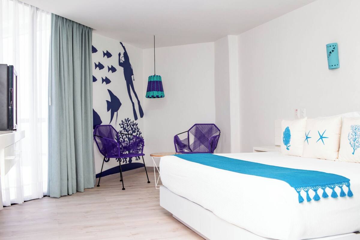 Moderni hotellihuone, jossa on sänky, työpöytä, tuoli ja seinä, joka on koristeltu kalakuvioisella seinämaalauksella.