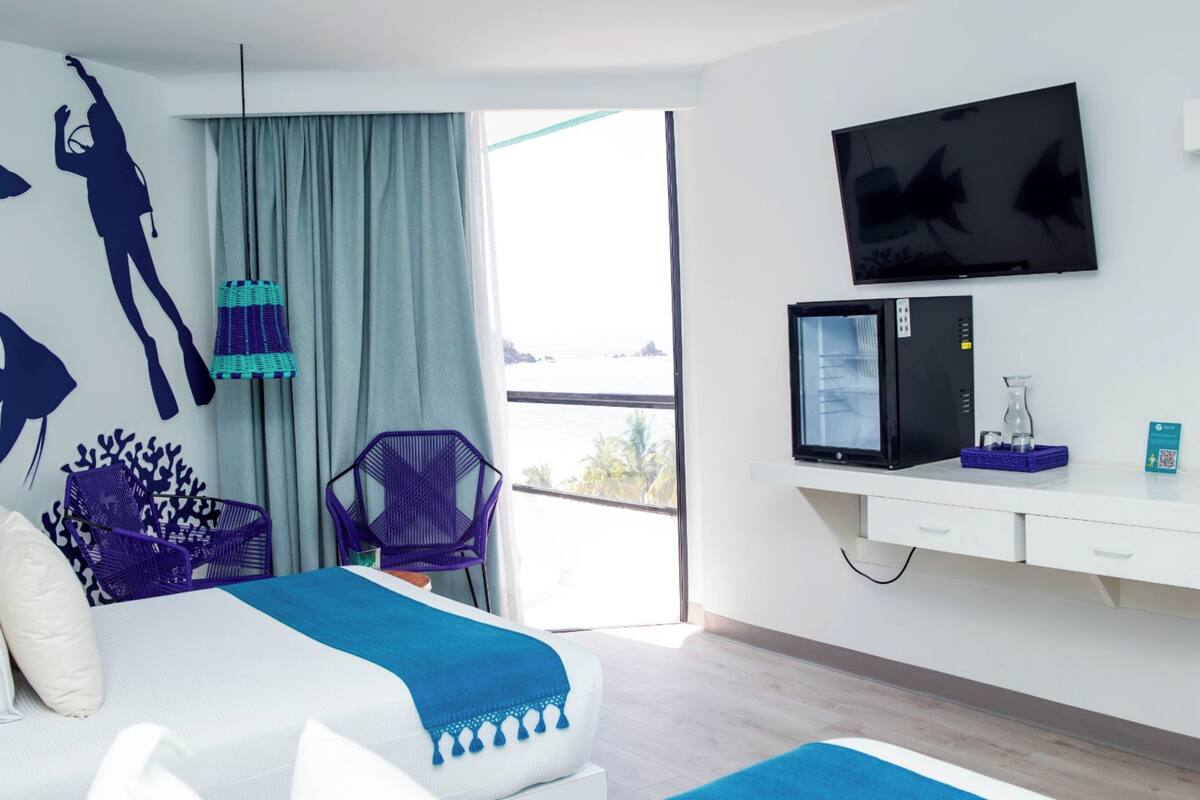 Moderni hotellihuone, jossa on sänky, televisio, mikroaaltouuni ja parveke, jolta on näkymä.