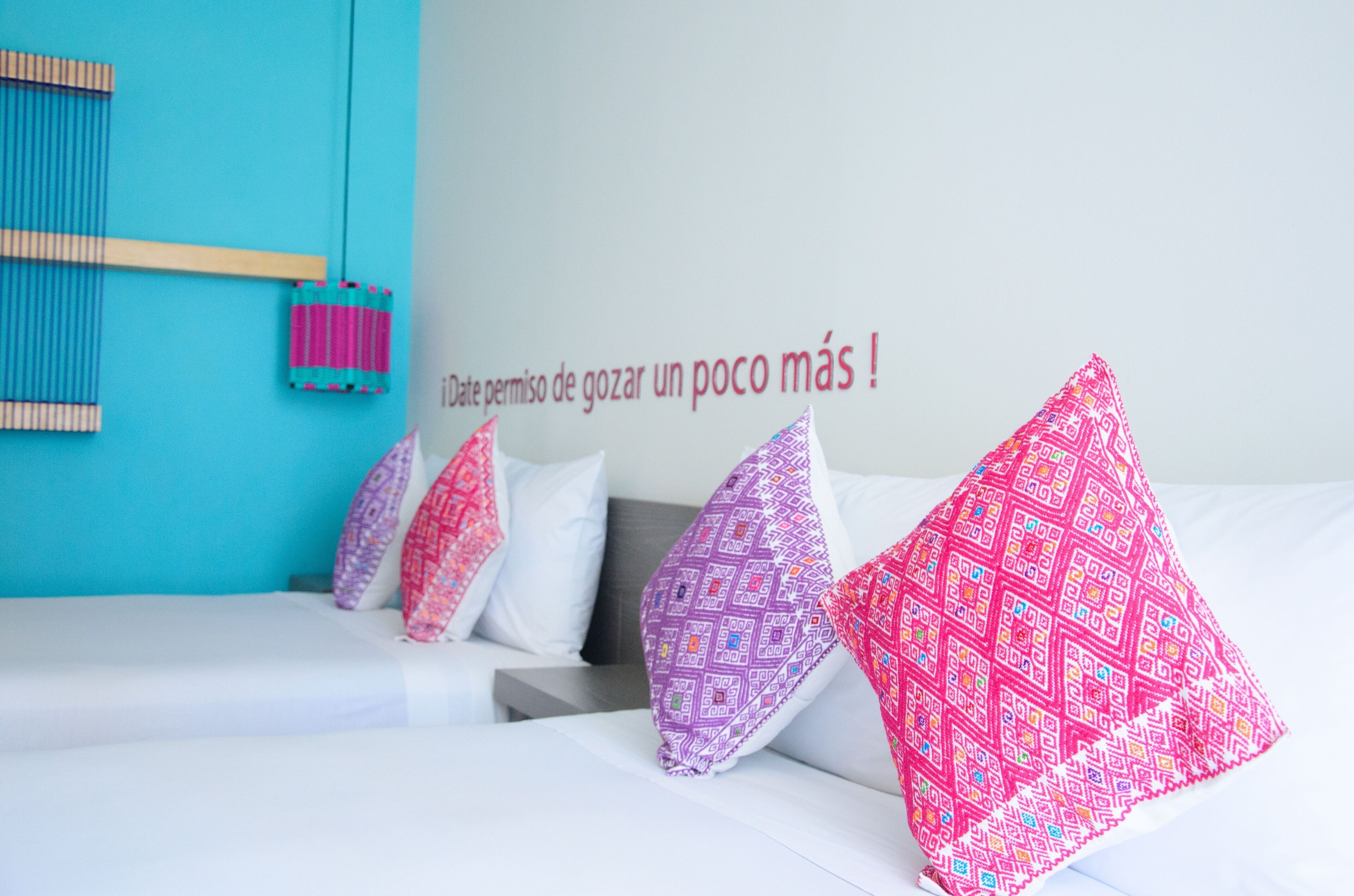 A hotel room with a bed, pillows, a wall with a message, and a blue wall with a hanging object.