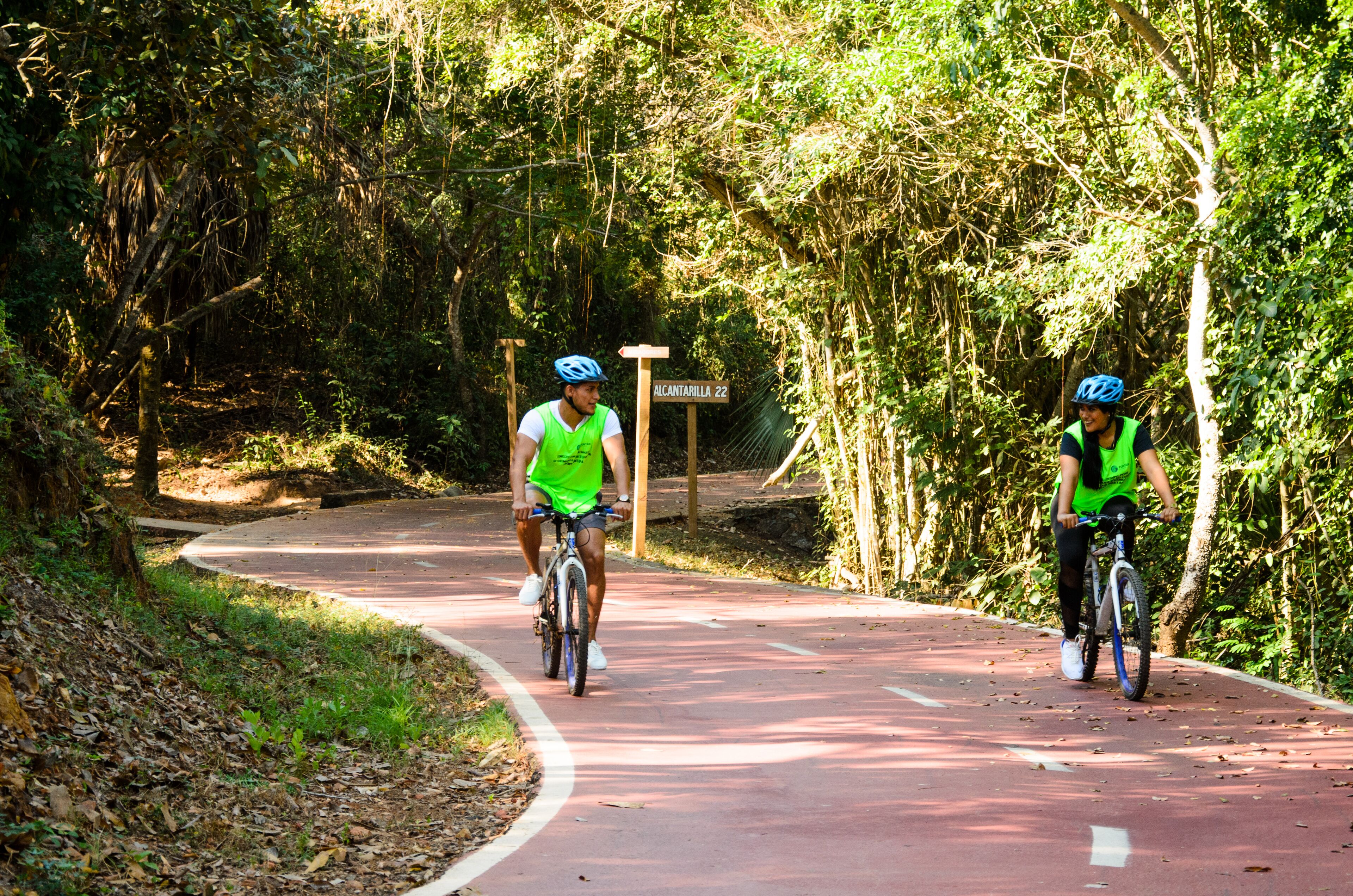 Dos ciclistas en un camino pavimentado bordeado de follaje denso.