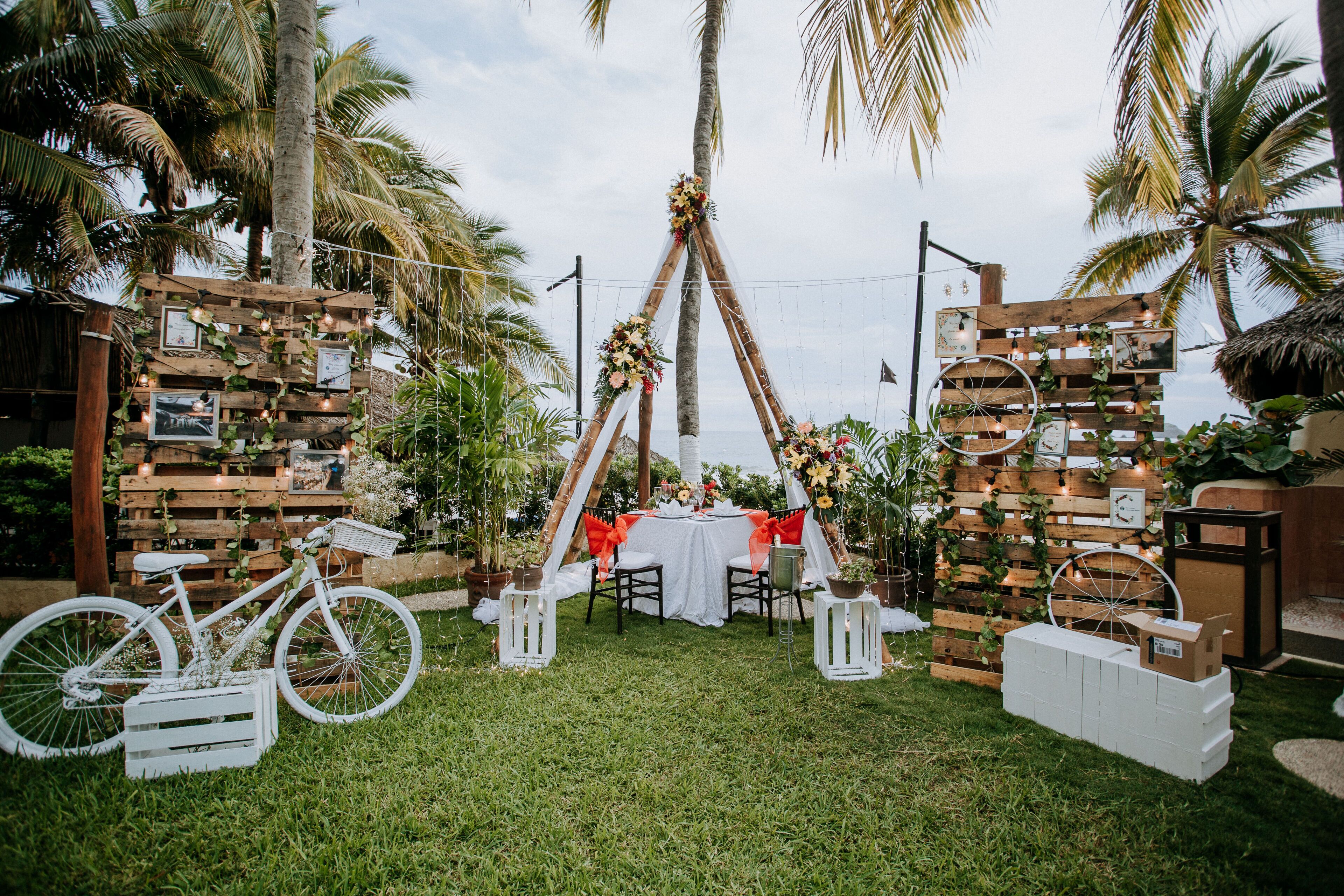 Un cadre extérieur rustique agrémenté d’une arche en bois, d’un vélo et d’une table dressée pour un petit rassemblement.