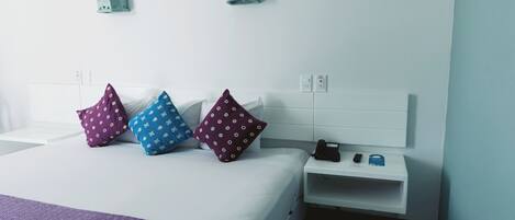 A hotel room with a bed, pillows, a nightstand, a phone, and a wall socket.