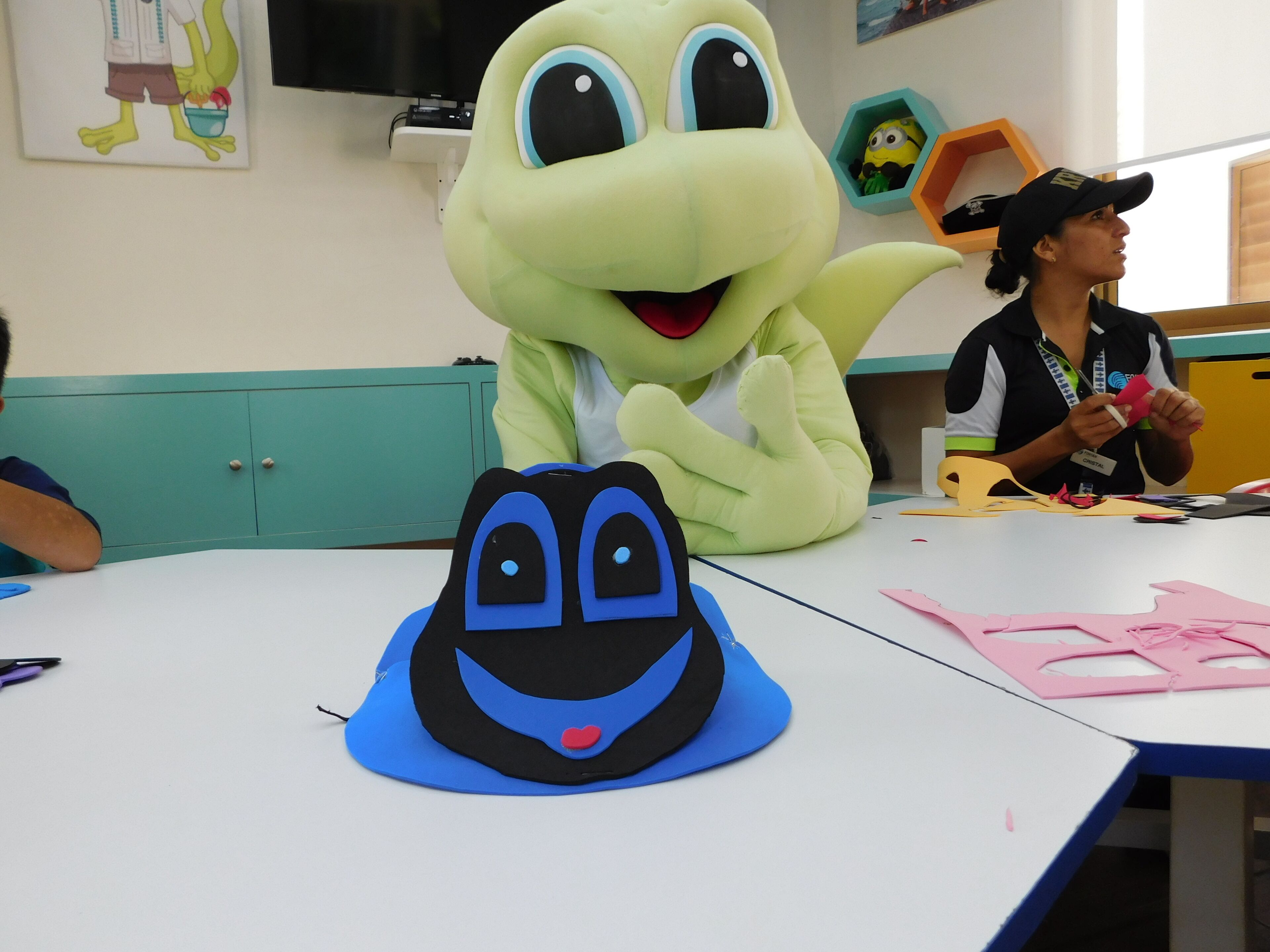Un salón de clases con un gran tótem verde, un sombrero azul y negro, y un juguete de Minion.