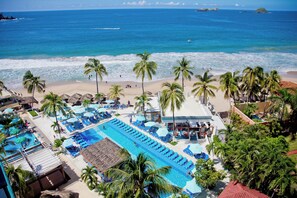 A resort with a swimming pool, beach, and palm trees.