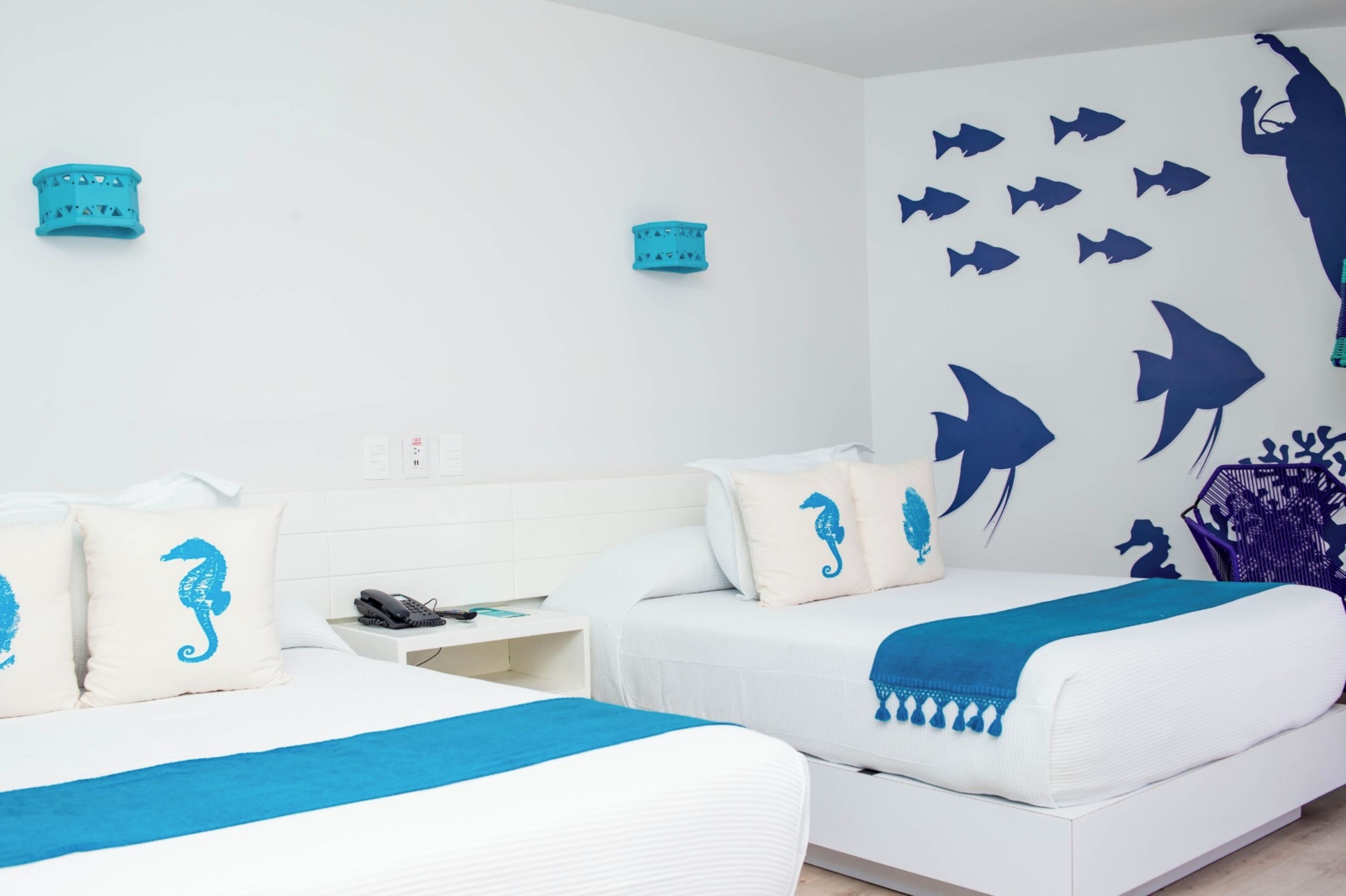 A hotel room with two beds, a nightstand, and a wall decorated with marine life silhouettes.
