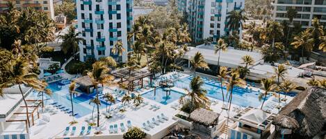 A resort with multiple swimming pools, palm trees, and beachfront seating areas.