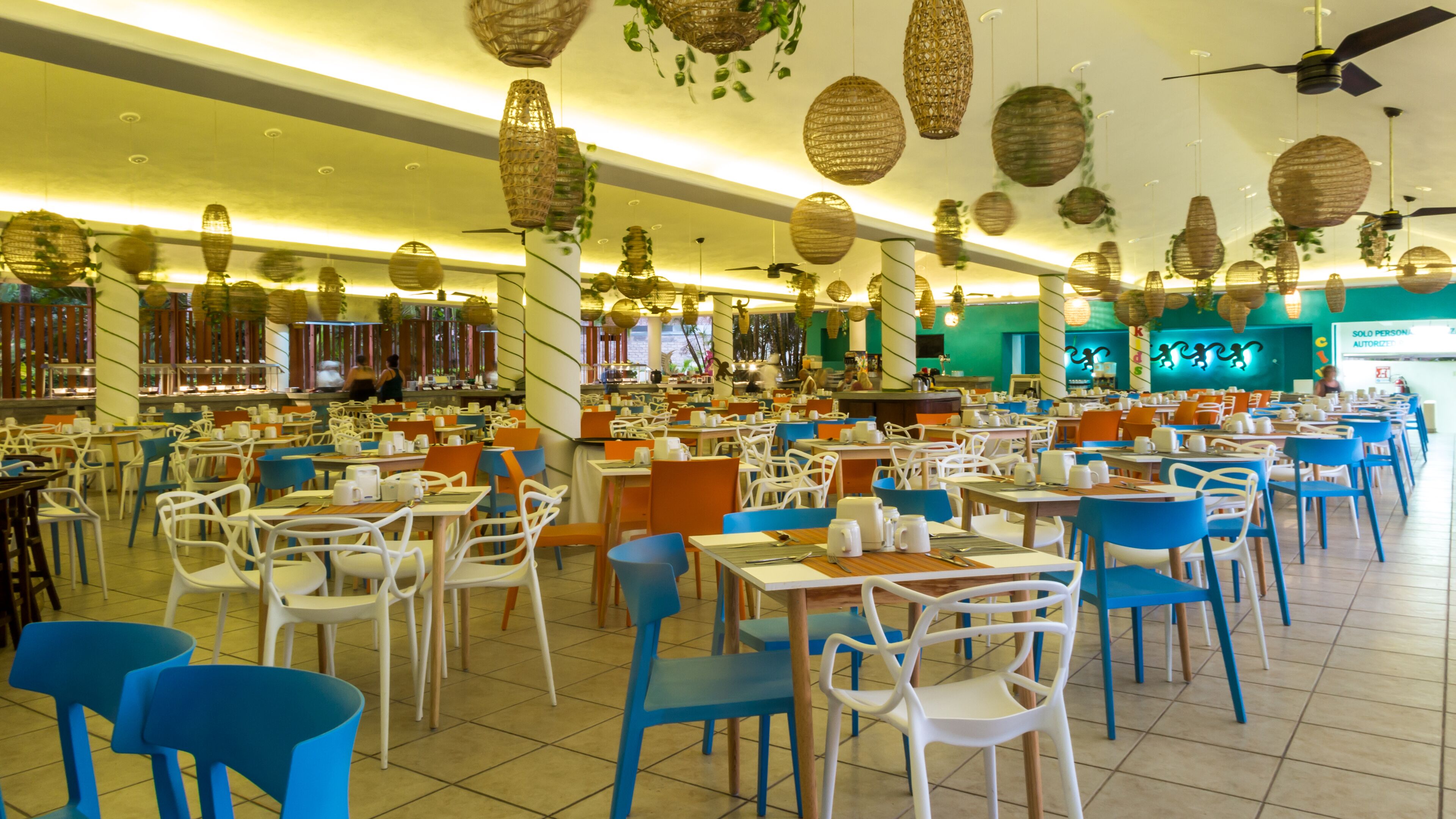 A spacious restaurant with high ceilings, hanging wicker lamps, and a variety of seating options including tables and chairs.