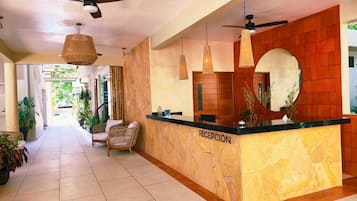 A reception area with a marble counter, wicker chairs, ceiling fans, and potted plants.