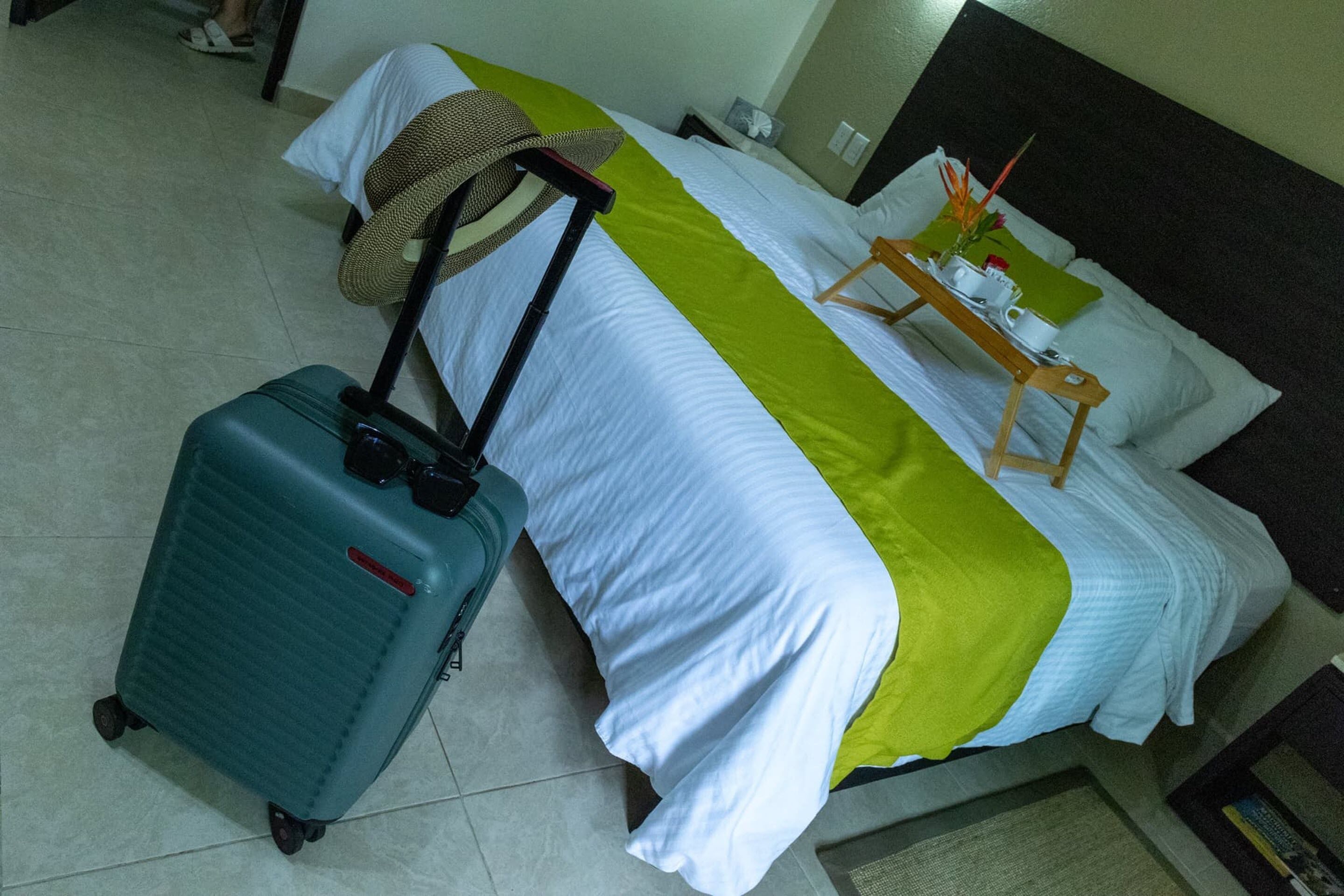A hotel room with a bed, a suitcase, and a hat on the bed.