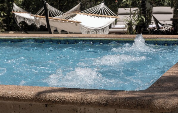 A swimming pool with water splashing, surrounded by lounge chairs and hammocks.