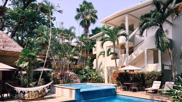 Un espace piscine équipé d’un hamac, de chaises longues et d’un bâtiment doté de balcons.