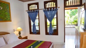 A bedroom with a bed, a nightstand, a lamp, and a view of the outside. - Hotel Flamboyan (Kuta)