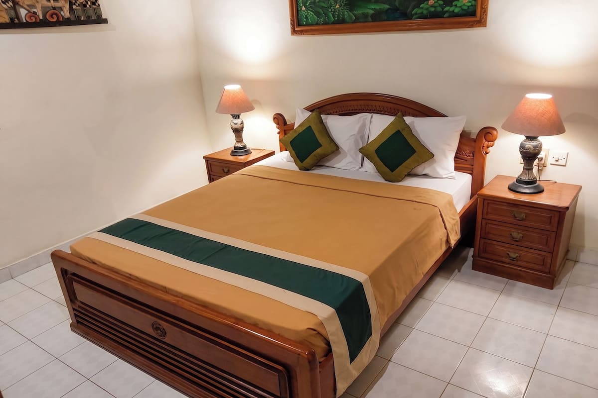 A neatly made bed with a wooden headboard, two bedside tables with lamps, and a wall-mounted painting.