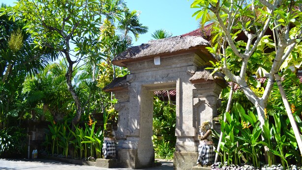 A stone archway with a thatched roof, surrounded by lush greenery and palm trees. - Hotel Flamboyan (Kuta)