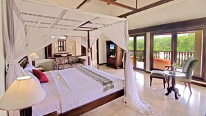 A spacious bedroom with a large bed, a sitting area with a chair and table, and a balcony with a view of the greenery. - Puri Bunga Resort & Spa (Ubud)