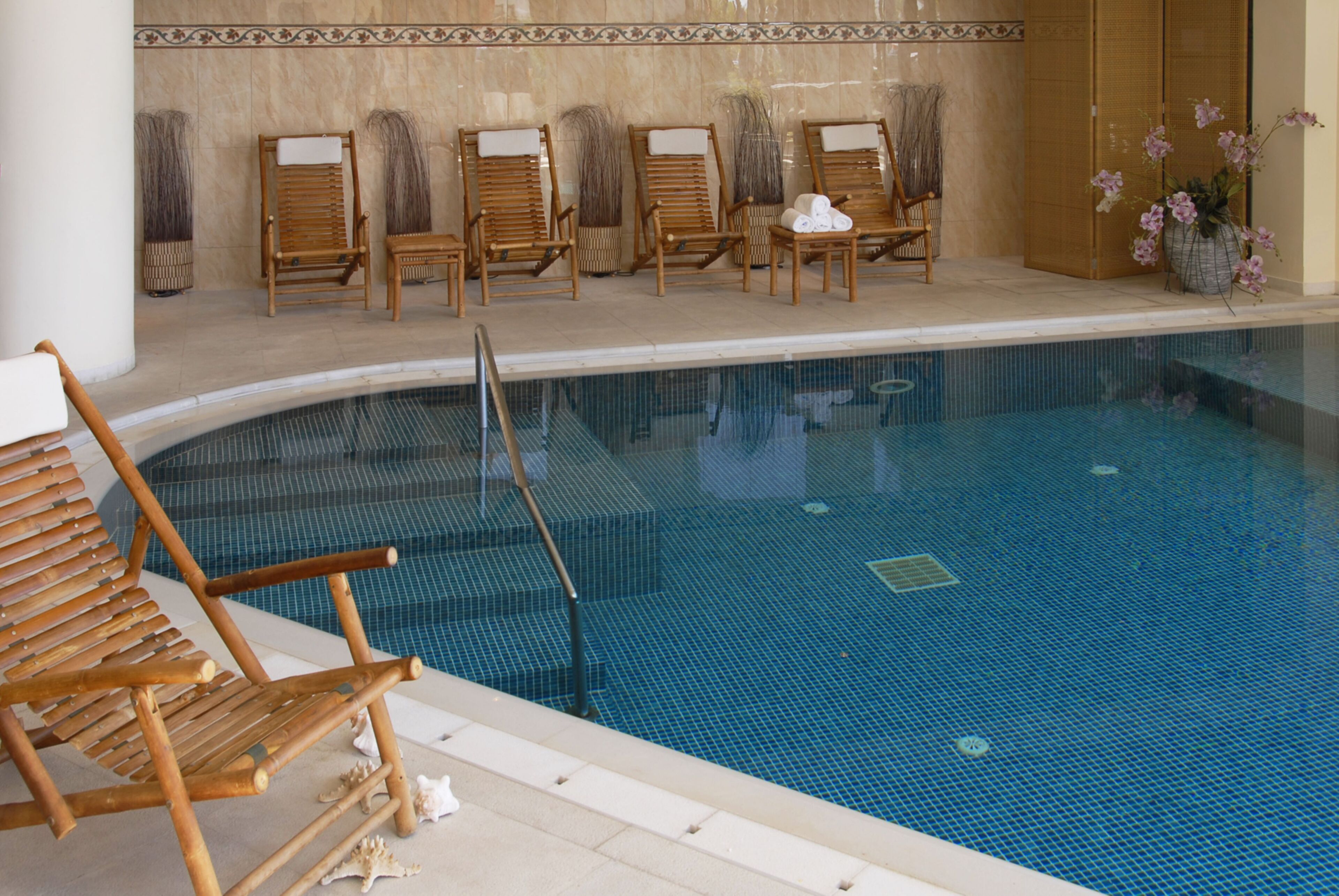 A pool area with wooden lounge chairs and a tiled floor.