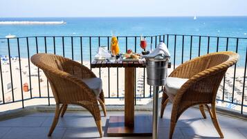 A balcony with wicker chairs, a table with breakfast items, and a view of the ocean.