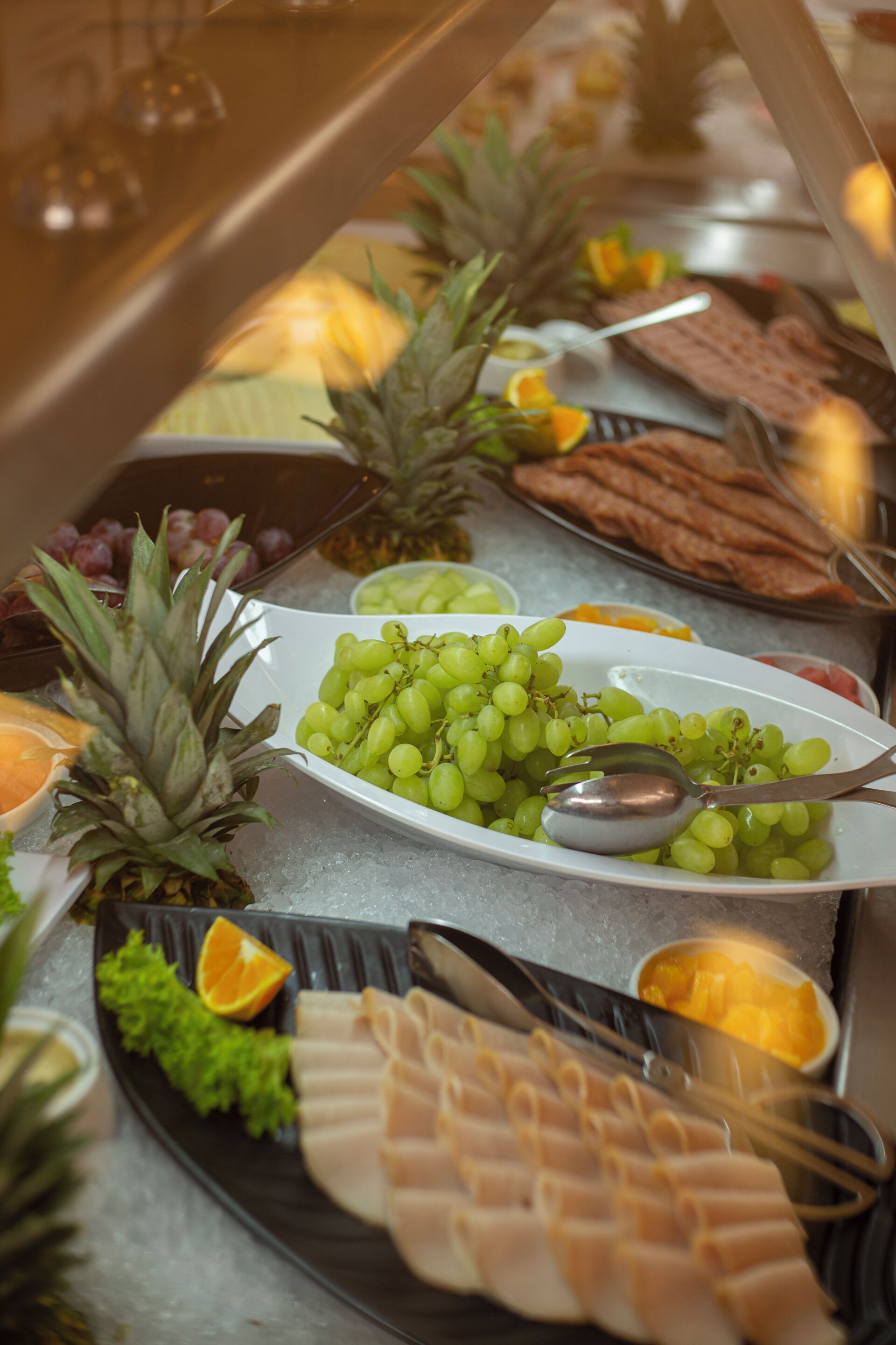 A buffet with various food items including grapes, pineapple, and sliced meats.