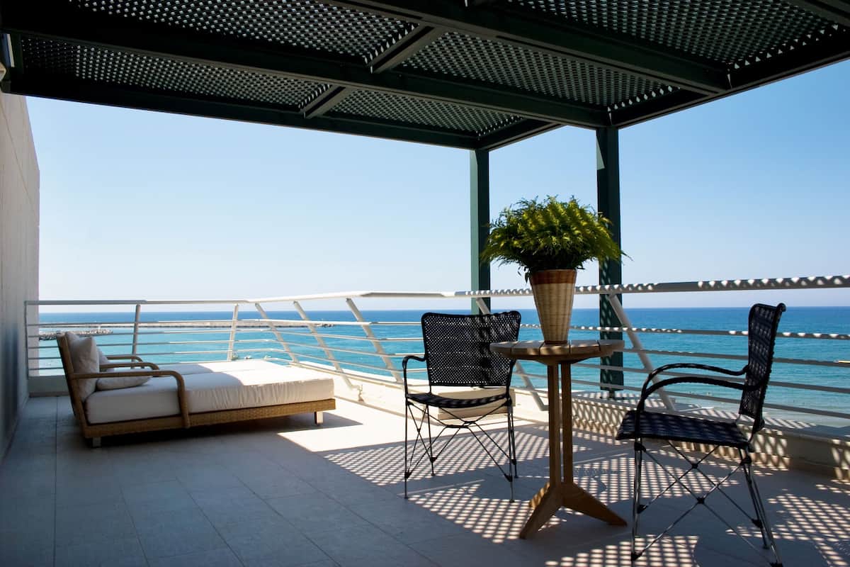 Varanda com sofá, duas cadeiras, uma mesa e planta em vaso, com vista para o mar.