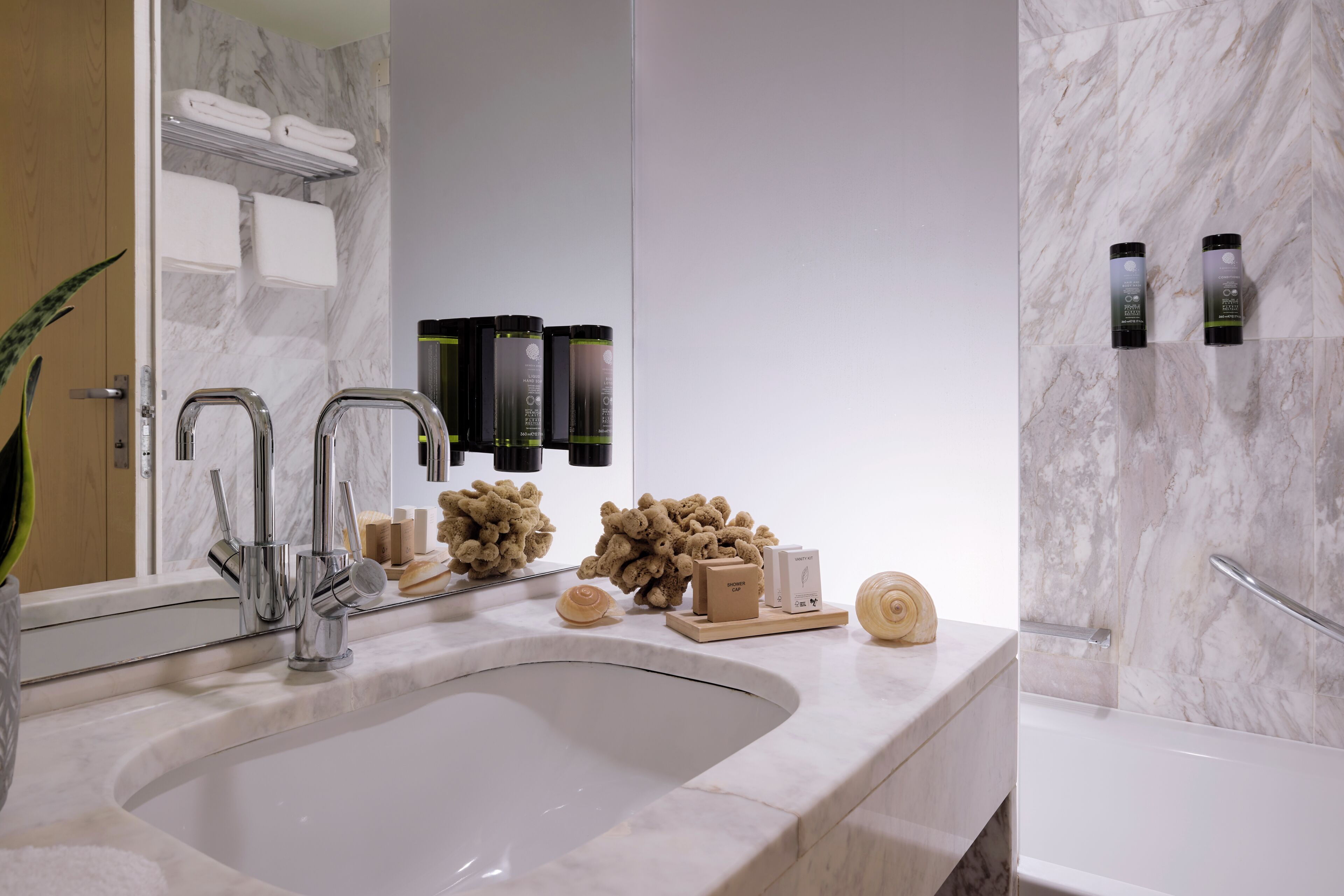 A bathroom with a marble sink, two faucets, a mirror, and toiletries on the counter.