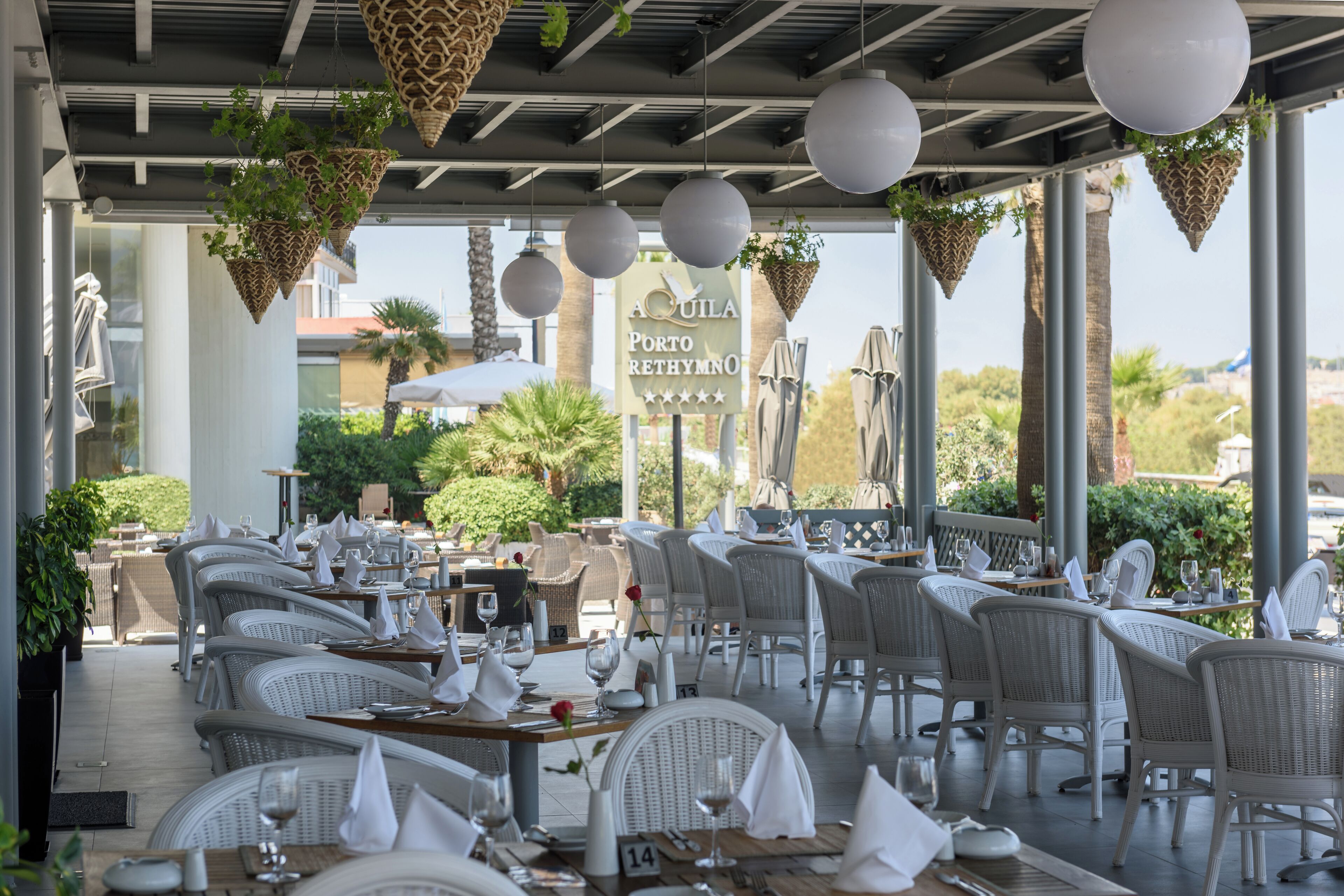 An outdoor restaurant with wicker furniture, hanging plants, and a sign reading "Porto Rethymno".