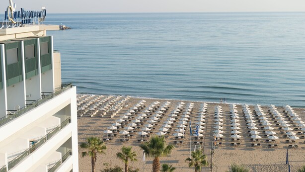 A beach with rows of umbrellas and a building with balconies overlooking the sea. - Aquila Porto Rethymno (Rethymno)