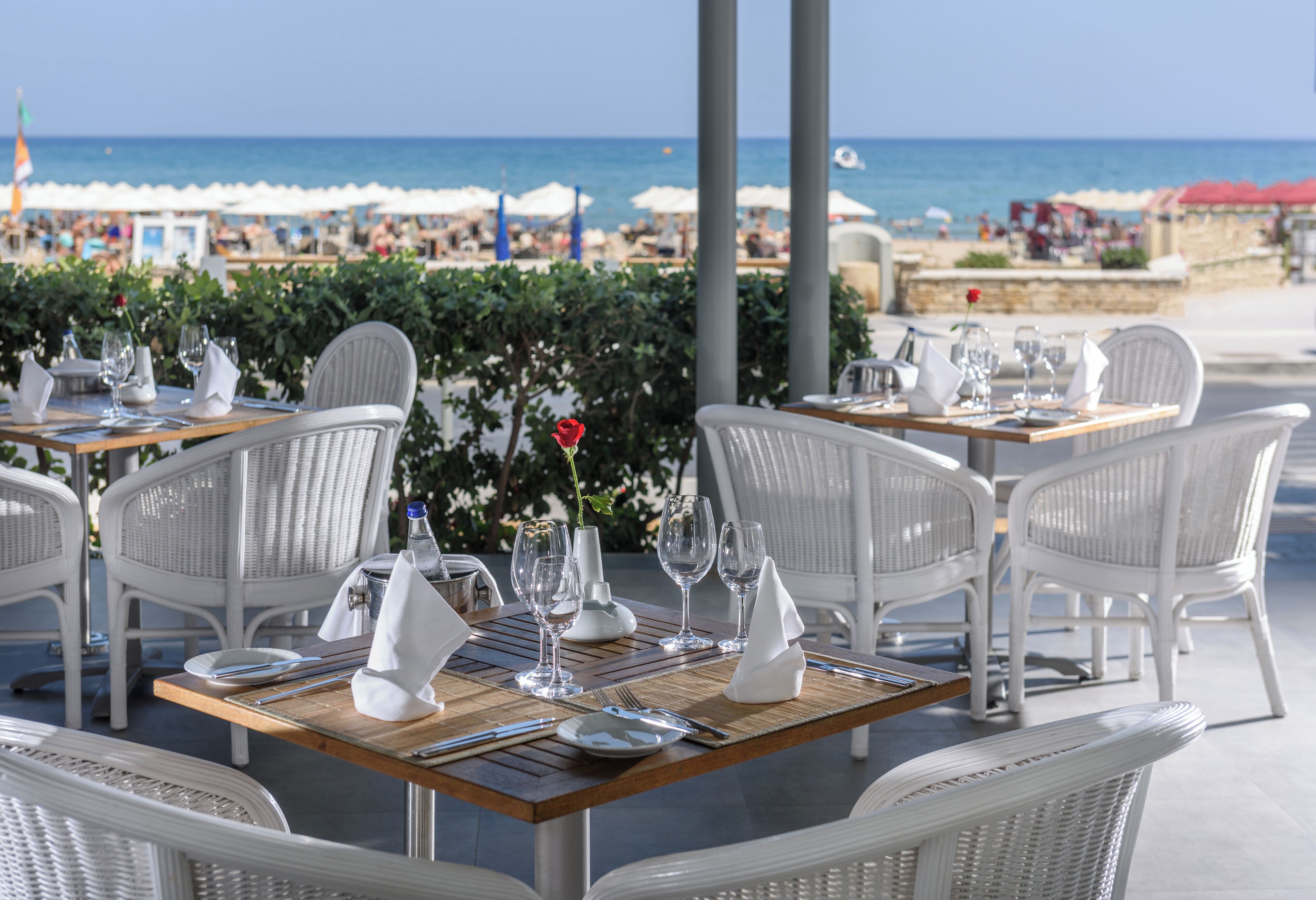 Un restaurante frente al mar con sillas y mesas de mimbre blanco dispuestas para comer, con vistas a la playa y al océano.