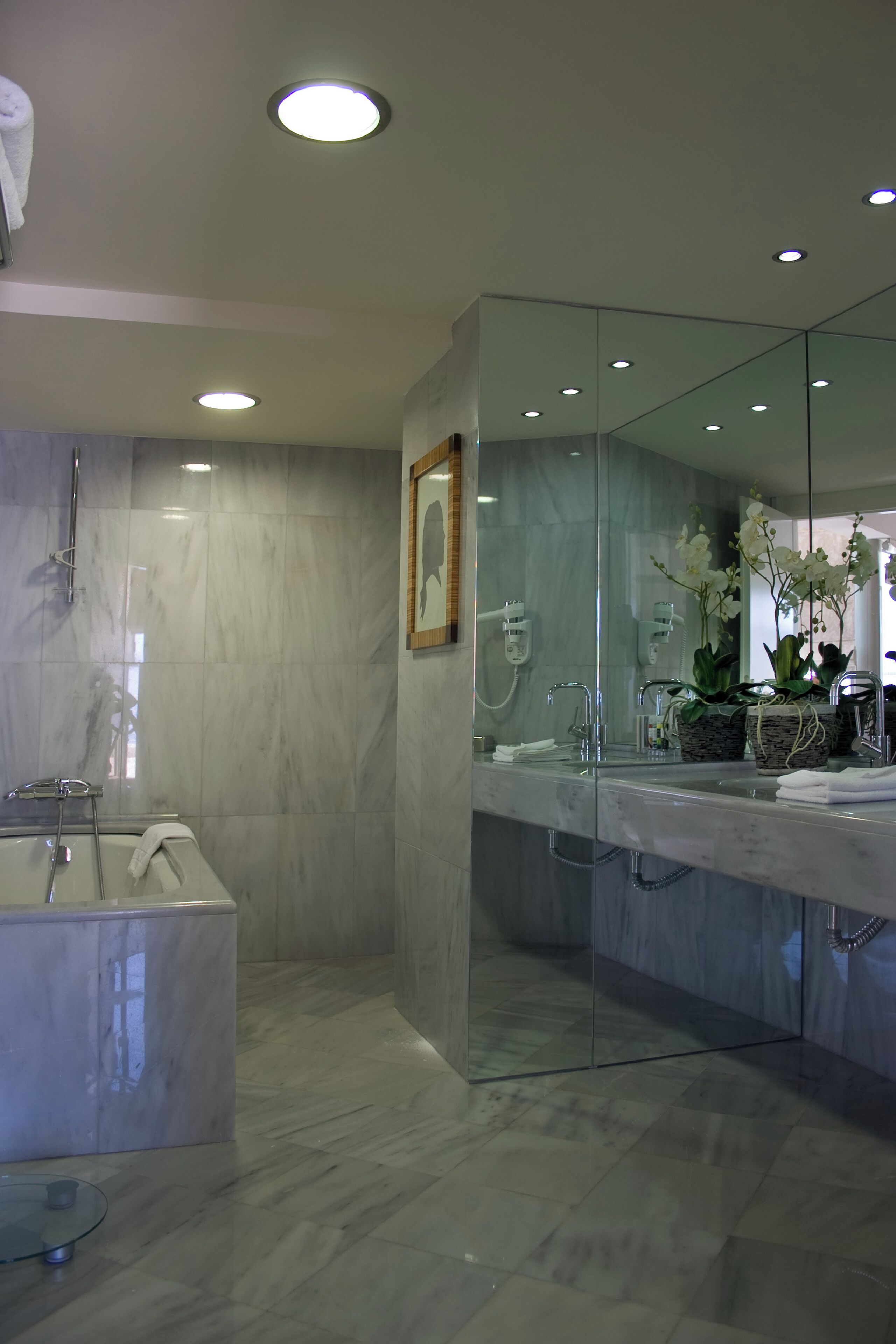 Un baño moderno con ducha envuelta en vidrio, un espejo grande y suelo de mármol.