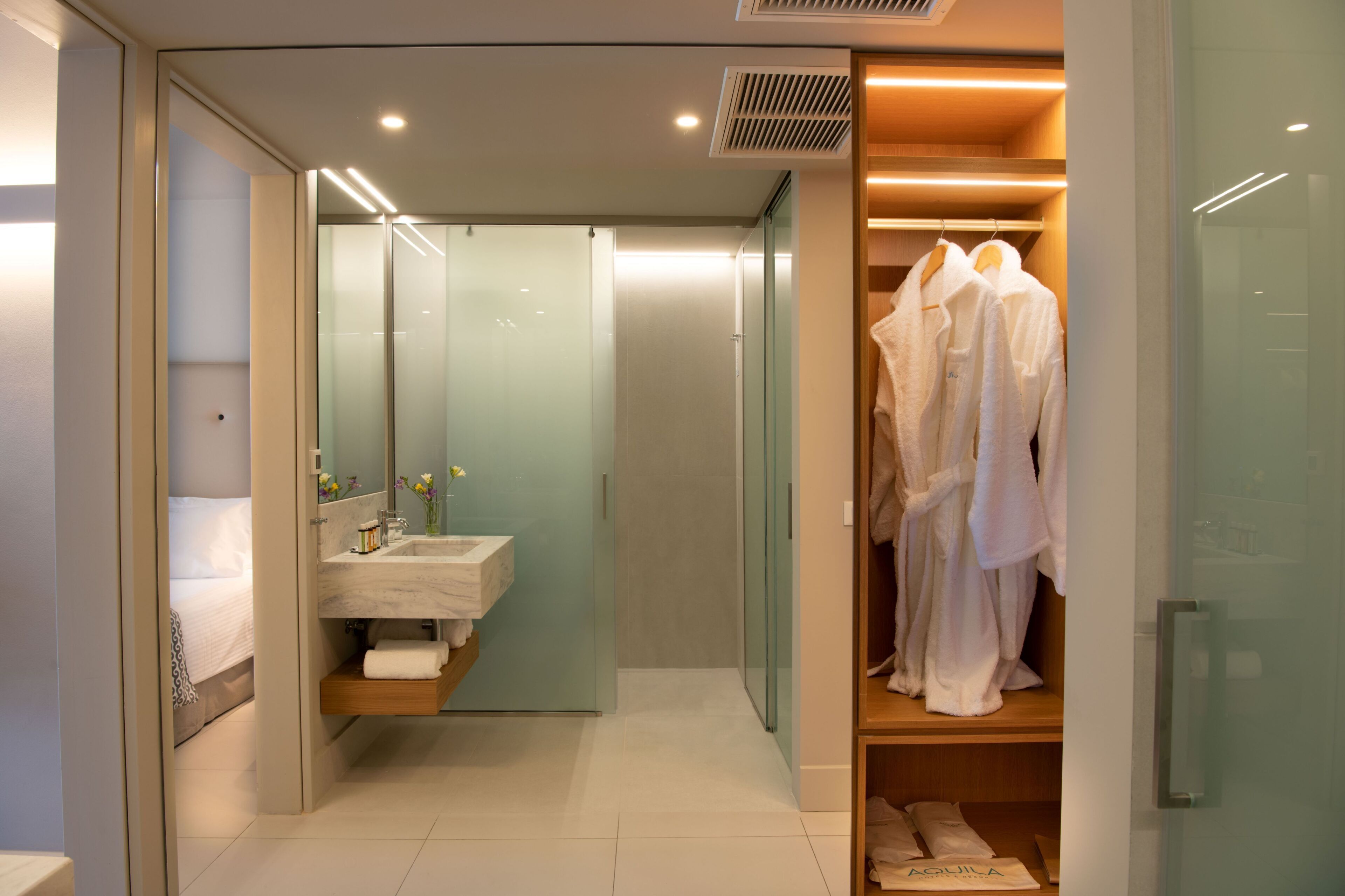 Een moderne badkamer met een douchecabine van glas, een wastafel met spiegel en een kledingrek voor gewaden.