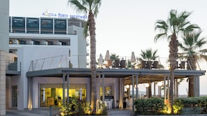 A hotel with a modern architectural design, featuring a covered outdoor area with seating and palm trees. - Aquila Porto Rethymno (Rethymno)
