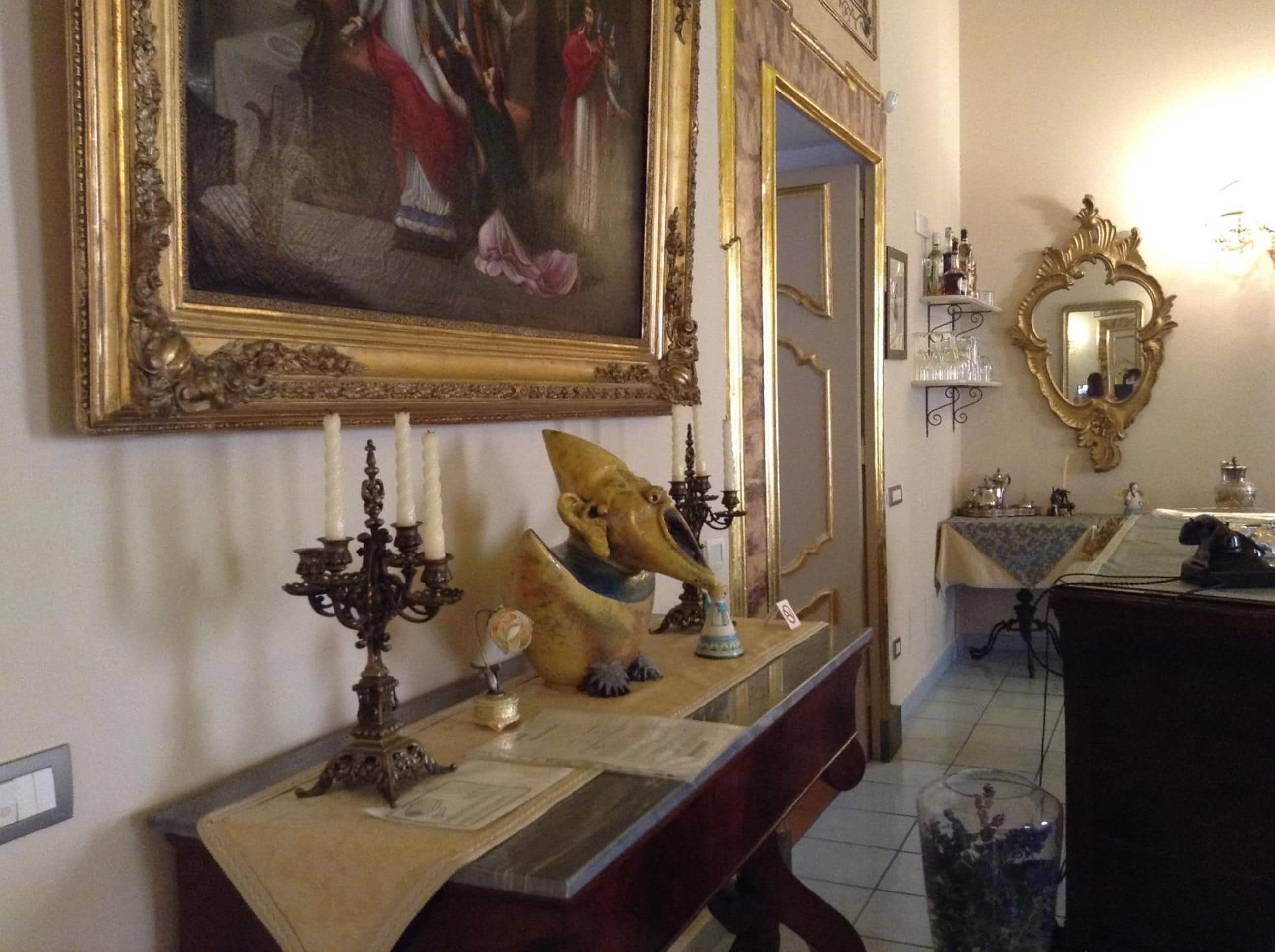Une pièce comprenant un grand miroir décoratif, un tableau encadré, un chandelier et un vase ornemental posé sur une console.
